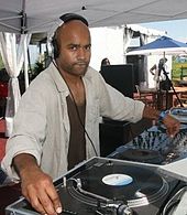 A man wearing a white shirt and headphones at a mixing table