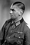 A man wearing a military uniform, facing left of the viewer. Dressed in German World War II Officer uniform with a neck order in the shape of a cross.