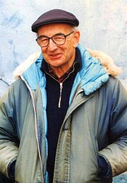 Photographie en couleurs d'un homme habillé d'un pull rouge, recouvert d'une parka bleue foncée et à la tête couverte d'un béret.