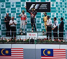 Sebastian Vettel celebrating a victory on a centre of a podium with two drivers either side of him