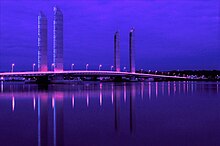 Photographie du pont Jacques Chaban-Delmas de nuit. La nuit est éclairée par le pont, qui reflète des couleurs violettes dans l'eau de la Garonne.