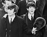 Photo en noir et blanc de John Lennon et Paul McCartney saluant une foule