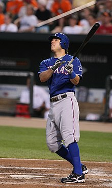 A man in a blue baseball uniform with a blue helmet watches the ball fly after swinging his black bat.