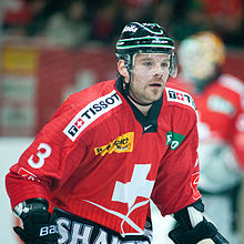 A Caucasian male ice hockey player shown from the knees up. He is wearing a red and white sweater with a black helmet.