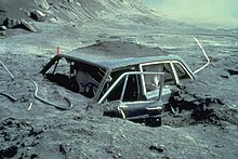 Heavily damaged car embedded in gray soil