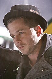 A picture of Ryan Tedder. He wears a coat and a hat.
