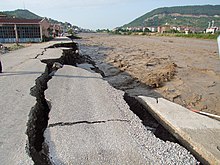 road with large cracks being washed away by a roiling brown river