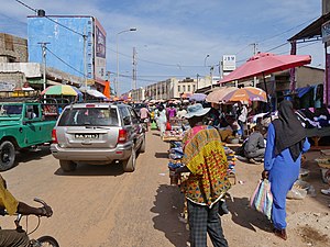 A busy street leading to a beige building. Vendors are on the side of the street.