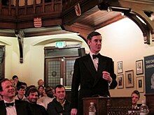 Image of Jacob Rees-Mogg, in a black suit and bow-tie, stood up to debate at the Cambridge Union