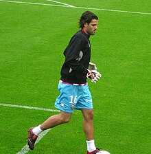 Photographie d'un joueur de football, un gardien de but, en short bleu ciel et avec une veste noir vu de profil.