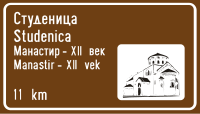 Panneau d'indication d'un lieu touristique complété par une indication de distance ainsi que par un message graphique