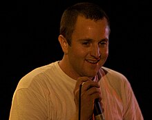 A man in a white T-shirt smiles and grasps a corded mic at its top