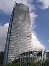 GGround-level view of a rectangular, glass high-rise; a smaller, circular building is in the foreground