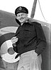 Informal portrait of grinning man in peaked cap and military uniform leaning against an aircraft fuselage