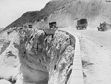 A road at the edge of a cliff with trucks driving both ways along it.