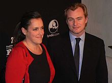 Christopher Nolan, on the right, is looking directly towards the camera as Emma Thomas is looking to her right.