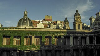 Vista desde el exterior del edificio con una galería rodeada de enredaderas, varias puertas. En la parte superio se ven 3 cúpulas.