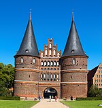 Medieval gate in red brick with two pointy towers
