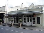 Single storey terraced shops; low pitched roof with large overhang; small-paned modern timber shop fronts on ceramic tiled base with splayed corners; recessed entrance doorways to shops. Double storey behind: double pitched fluted galvanised iron sheeting. Type of site: Commercial Current use: Personal services.