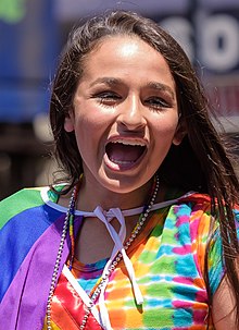 Jennings, dressed in LGBT pride wear, smiles to parade outlookers from a convertible car.