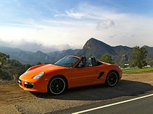 Photo de la Boxster "Limited Edition", orange avec des jantes noires, arrêtée sur le bord d'une route.