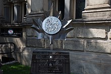 silver metal sculpture shaped like a coin situated outside a building