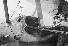 Photographie en gros plan du flanc d'un avion. Un homme portant une casquette et des lunettes de protection sur le front est assis dans le cockpit.