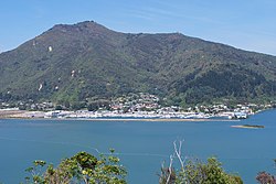 The waterside township is visible in the distance, seen from across the water. It has a marina in front, and sharp hills rising immediately behind it