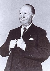 Black-and-white photo of an older man dressed formally in a dark suit, white shirt, and tie