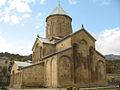 Monastère en forme de temple en croix avec arcatures en pierre de couleur sable et surplombé par un clocher surmonté d'une croix orthodoxe.