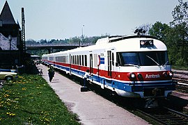 A white passenger trainset with red and blue horizontal stripes on the side