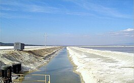 A conduit with water, a small earth dam head, and a lake