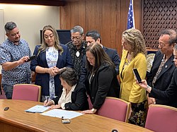 Governor Lou Leon Guerrero Signs Bill 181-35 into law as senators observe from behind.