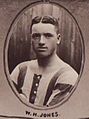 Head and upper torso of a stocky white man with dark hair parted in the middle. He is wearing a sports shirt with broad stripes