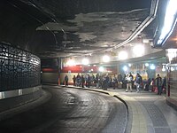 Passengers waiting in Harvard bus tunnel, upper level. Central atrium is visible though windows at rear.