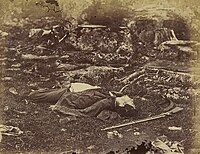 Black-and-white photograph of a dead soldier, lying on his back in a flat field.