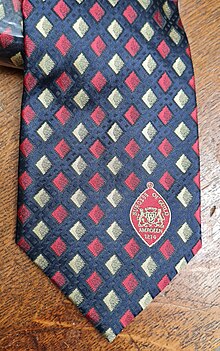 a necktie with a red on blue pattern and a badge showing the date of founding: 1214