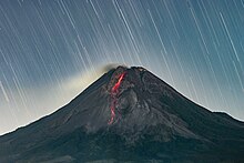 Volcan noir, fendu d'une rigole de lave rouge, de nuit, avec un ciel étoilé pris en pause longue.