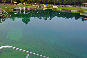 A pond with bluish-green water, several buoys and recreational facilities around it, seen on a cloudy day