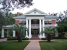 an old southern neoclassical-styled mansion with manicured lawn and palm trees