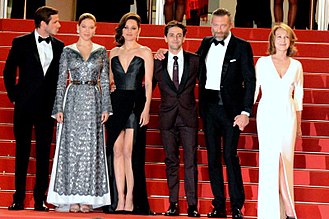 Photographie au format paysage et en couleurs de plusieurs personnes en tenue de gala, posant en souriant sur un tapis rouge.