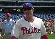 A man wearing a white baseball uniform and blue baseball cap with red brim and a red "P" on the face