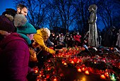 People place candles at a statue depicting a young girl clutching a handful of wheat