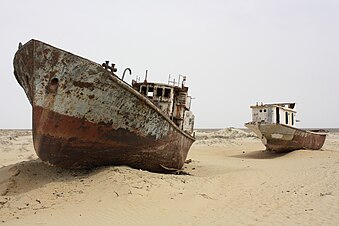 Two rusted fishing boats sit on a sandy terrain, with no water in sight