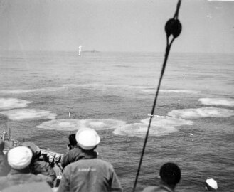 Sailors observe a ring of small circular waves from the impact of Hedgehog bombs into the water
