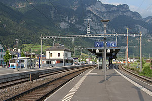 Three tracks, platforms, and a squat two-story building with mountains behind them