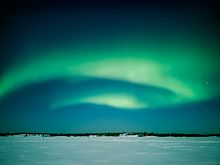 Curtains of greenish light in the night sky over a flat, snowy landscape