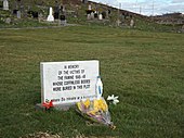 Épitaphe de marbre posée sur un terrain engazonné au milieu d'un cimetière.