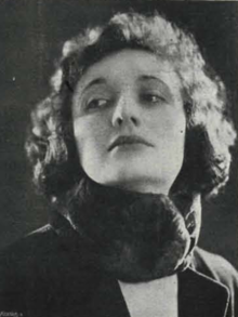 A white woman, head tilted back, with curly hair, wearing a dark scarf around her neck