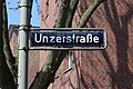 Leichte Abwandlung der Schrift von Holstenstraße beim Schild Unzerstraße, kenntlich am mittleren Strich des kleinen a, der sich nach links hin nach oben wölbt; entsprechend ist die rechte untere Ecke des unteren Lochs nach oben gezogen